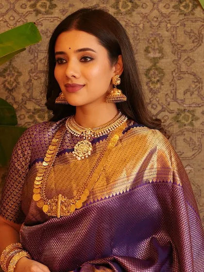This bride in a purple Kanjeevaram saree showcases a look of understated elegance. The makeup is natural, with highlighted eyes, letting the rich saree and traditional gold jewellery take center stage.