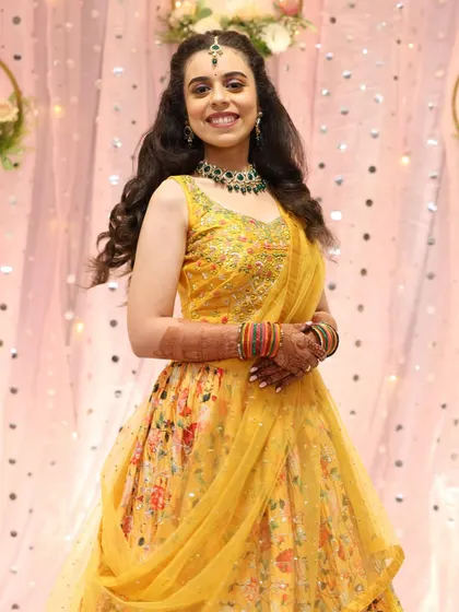 A full-length shot of the bride's cheerful sangeet outfit. The hairstyle is kept soft with curls to match the playful vibe.