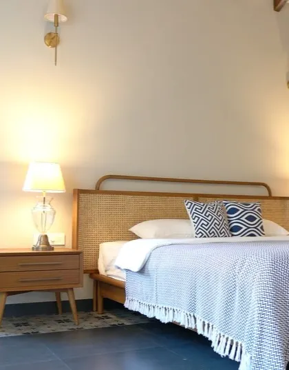 Another view of the Goa villa bedroom, highlighting the custom bed with its rattan headboard and the warm, ambient lighting from the bedside lamps.
