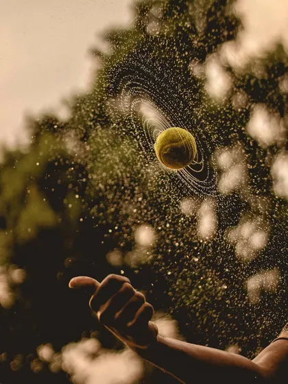 A wet tennis ball is captured spinning in mid-air, creating a perfect spiral of water droplets around it like the rings of Saturn. This is a fantastic high-speed photograph that freezes a cool physics moment.