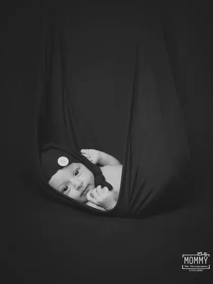 "Hang in there handsome." This is a classic and artistic newborn pose, with the baby safely cradled in a hanging sling. The black and white edit gives it a timeless and dramatic feel.