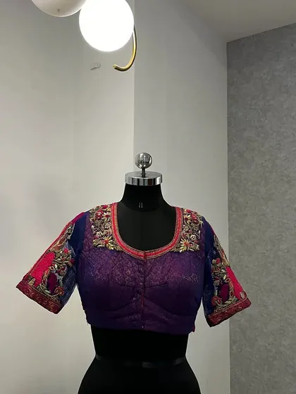 This royal blue and purple blouse is crafted from a delicate net fabric. It features intricate zari and knot work on the sleeves and neckline, offering a modern yet traditional look for any wedding or party.