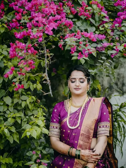 A serene portrait of a Maharashtrian bride in a purple saree, standing against a backdrop of bright pink bougainvillea.