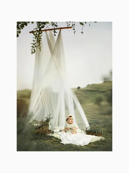 The baby sits up and looks around, her curiosity sparked by the beautiful outdoor setting. The soft, diffused light and natural surroundings make for a truly angelic portrait.
