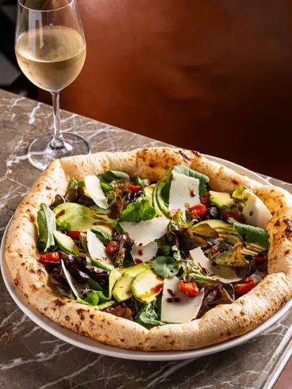 A pizza topped with fresh salad and shaved parmesan, paired with white wine. This composition suggests a sophisticated, light pairing.