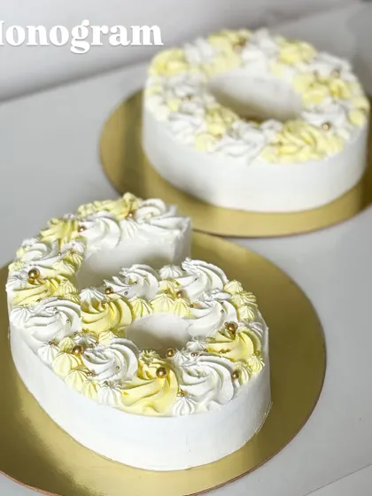 A monogram cake is a perfect way to celebrate a milestone. These "G" and "O" cakes are decorated with beautiful yellow and white piped frosting and delicate gold pearls.