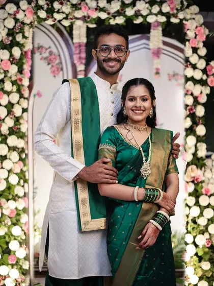 A full-length portrait of an engaged couple standing before a beautiful floral arch.