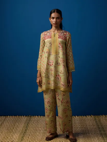 A clean, full-length e-commerce style shot. The model's direct gaze and simple pose against a solid blue background make the floral-printed kurta set the hero, allowing customers to see the full outfit clearly.