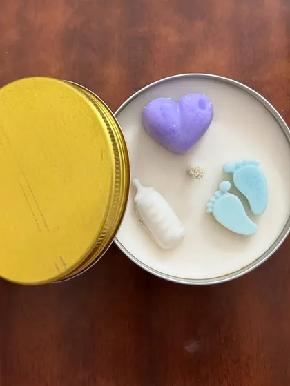 Another look at the baby-themed tin candle, this time with the lid off to the side. The tin container makes it a durable and travel-friendly gift.