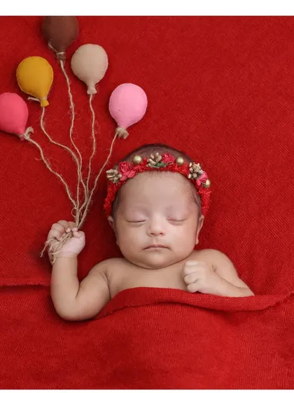 A pop of color. This baby girl holds a bouquet of felt balloons, adding a whimsical touch to a simple portrait on a vibrant red background.