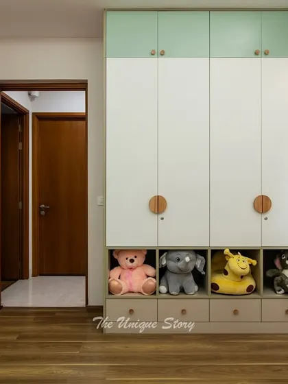 A view of the custom wardrobe in the nursery, featuring a mix of closed cabinets and open shelves at a child-friendly height. The two-tone finish and round wooden knobs add a playful and modern touch.