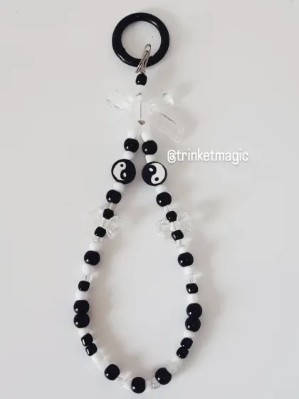 This phone charm features a balanced mix of black and white beads with yin-yang symbols and clear bows.
