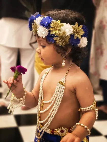 A quiet moment where the child, dressed for Janmashtami, curiously examines a flower. These small, unscripted interactions make for the most memorable and authentic kids' portraits.