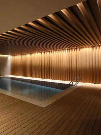 Another view of this luxurious indoor pool area, highlighting the warm ambient lighting and the floor-to-ceiling wood cladding on the walls, creating a spa-like atmosphere.