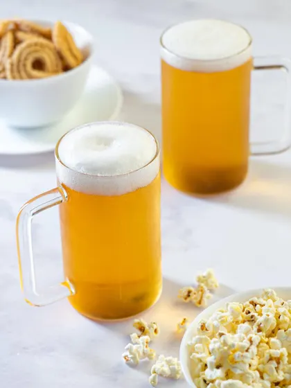 Beer mugs styled with popcorn and other snacks, suggesting a casual, relaxed occasion.
