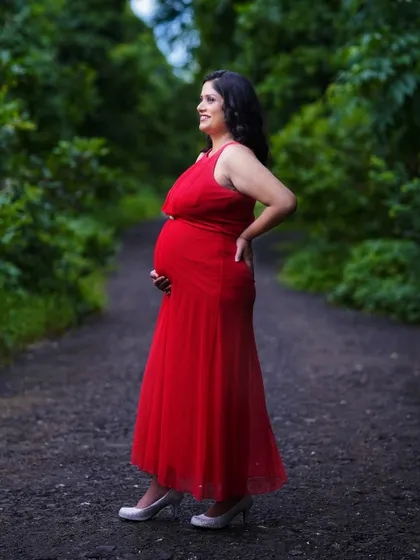 A side-profile shot of the mother-to-be, showcasing her baby bump against a beautiful, soft-focused green background. This pose is perfect for highlighting the pregnancy silhouette.