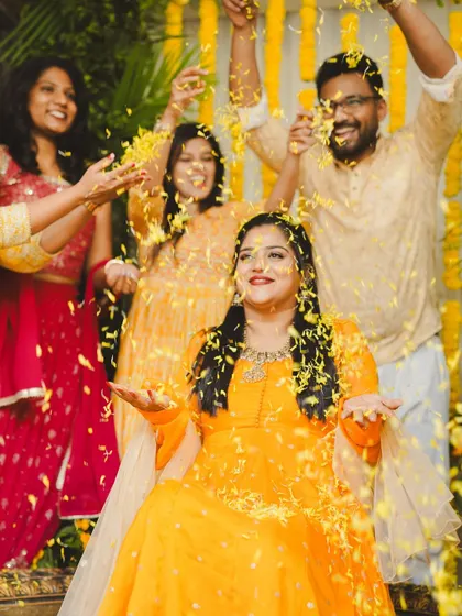 Friends and family shower the bride with flower petals during her Haldi. Our backdrop of marigold strings and palm leaves creates a perfect photo opportunity.
