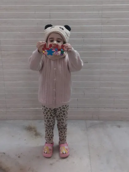 A proud little girl holding up her colorful popsicle stick craft. This activity helps with color recognition, patterns, and fine motor skills.