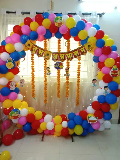 A traditional Annaprashan (first rice-eating ceremony) decoration. A circular balloon arch in primary colors frames a backdrop with marigold garlands and festive banners.