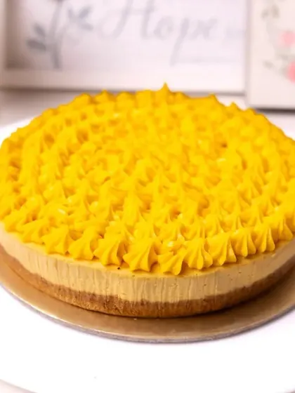 A vibrant and fresh baked mango cheesecake with a beautiful piped mango frosting.