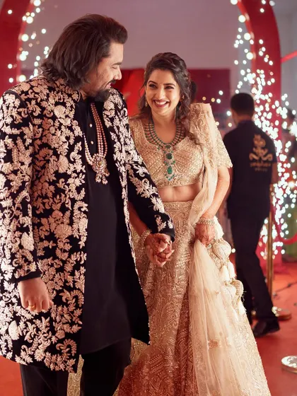For this joyous occasion, I designed a custom black sherwani jacket featuring intricate, contrasting floral embroidery. It creates a powerful yet elegant statement, perfectly harmonizing with the bride's golden lehenga for a stunning couple's entrance.