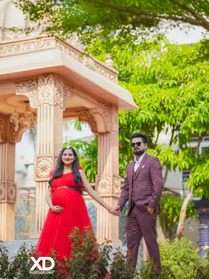 A stylish couple holding hands in a beautiful garden with an elegant gazebo in the background.