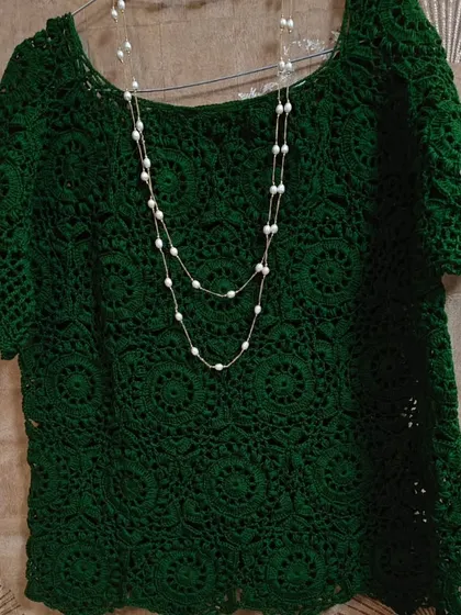 The green lace top styled with a simple pearl necklace. The classic scoop neckline and elegant drape make it a piece that can be dressed up or down for any occasion.