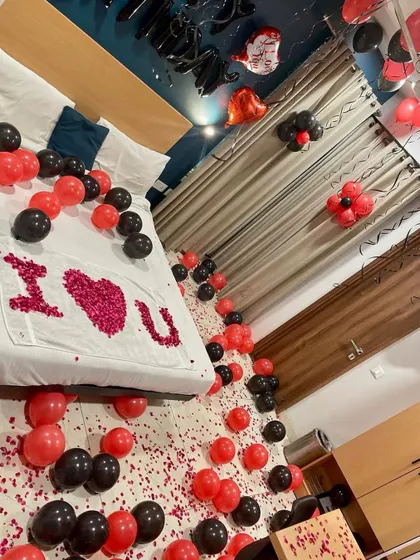 A full view of a romantic room decoration, with red and black balloons scattered on the floor and an "I love U" message on the bed.