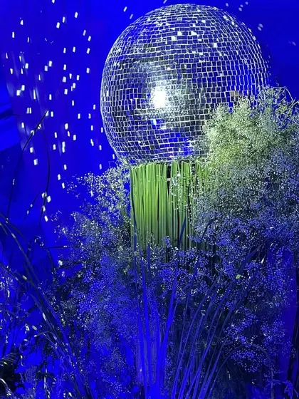 A close-up of a disco ball centerpiece from the 65th birthday party. The shimmering ball sits atop a cloud of baby's breath, perfectly capturing the event's elegant and celebratory "starry night" theme.