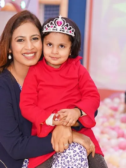 A mother and her daughter, the birthday princess, smile for the camera while sitting in the ball pit.