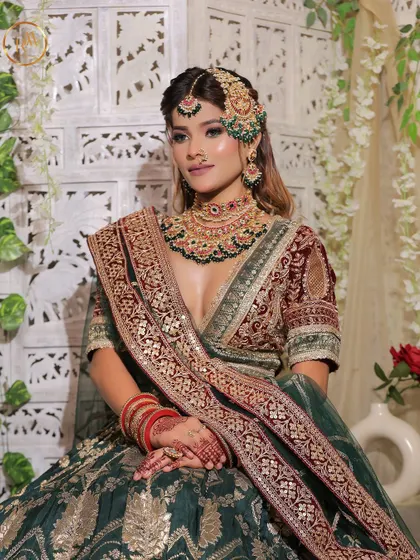 A full seated view of the green and maroon lehenga, showing the beautiful contrast and heavy embroidery.