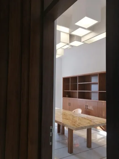 A glimpse into a corporate office we designed, revealing a modern meeting space. The room features a heavy marble table, clean wooden cabinetry, and a custom ceiling light installation, creating a professional and design-forward environment.