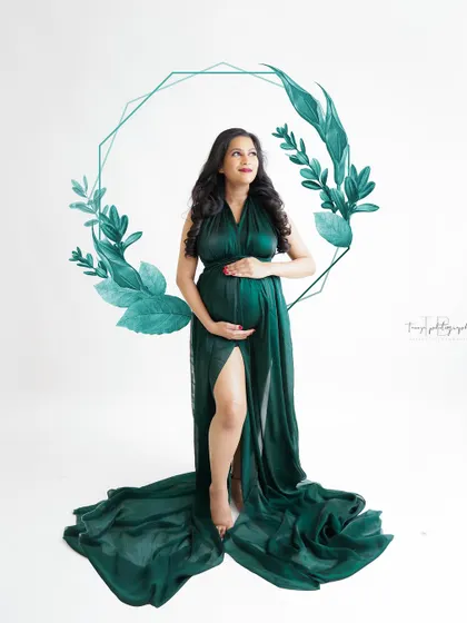 A modern and artistic portrait. The mom-to-be stands in a flowing green gown, framed by a graphic leaf design.