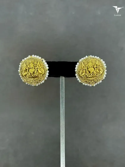 A closer look at the divine craftsmanship of our 22kt gold Maa Laxmi earrings. Set on a stand, the intricate details and surrounding pearls are clearly visible, showcasing a timeless design.