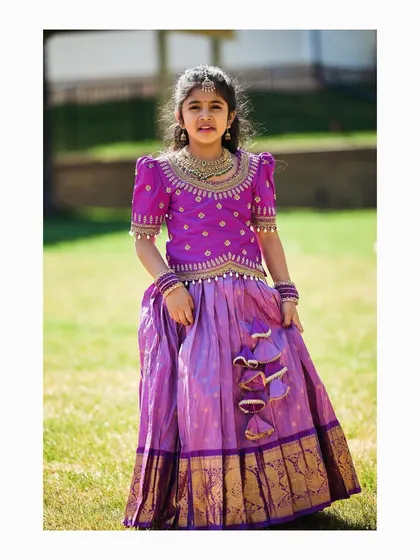 This young lady is a picture of grace in her lilac pattu lehenga. The outfit is completed with a purple blouse featuring detailed maggam work, perfect for a wedding or cultural event.