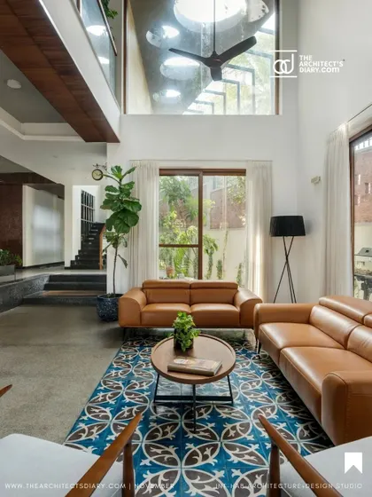 The living room is bathed in white, which contrasts with the warm wood tones and the vibrant blue of the traditional rug. The high ceiling with a circular skylight adds architectural interest and brings in abundant daylight.