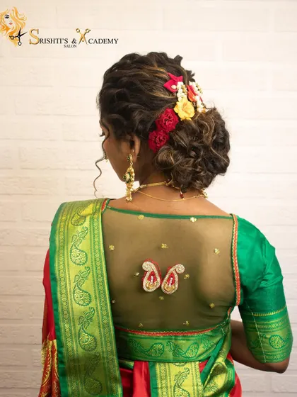 The back view of a beautiful Maharashtrian bridal hairstyle. The messy bun is adorned with fresh flowers, perfectly complementing the sheer-back blouse design.