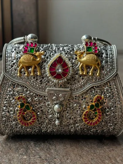 This is where tradition meets trend. A close-up of our bespoke fusion clutch, featuring intricate silver filigree work with gold plating and colourful stone embellishments like camels and paisleys. It’s a statement piece that tells a story.
