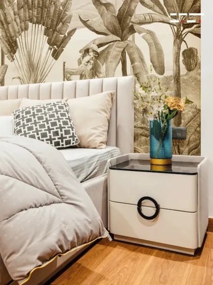 A detailed shot of the bedside area, showing the elegant white nightstand with a circular handle, a delicate vase, and the beautiful texture of the botanical wallpaper.
