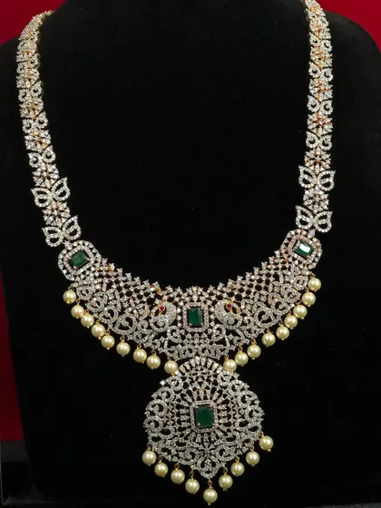 A beautiful long CZ haram with emerald accents and pearl drops. This can be worn alone or layered with a choker for a more grand look.