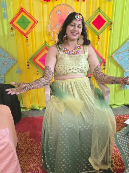 A happy client showing off her full-arm mehandi against a colorful Haldi backdrop. The traditional design is perfect for wedding festivities.