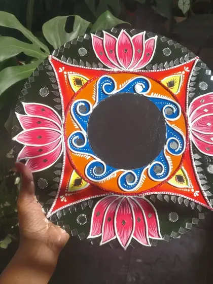 A beautiful Lippan art mirror with a lotus theme. The vibrant pink and orange colors are complemented by the traditional mirror work, making it a functional and decorative piece.