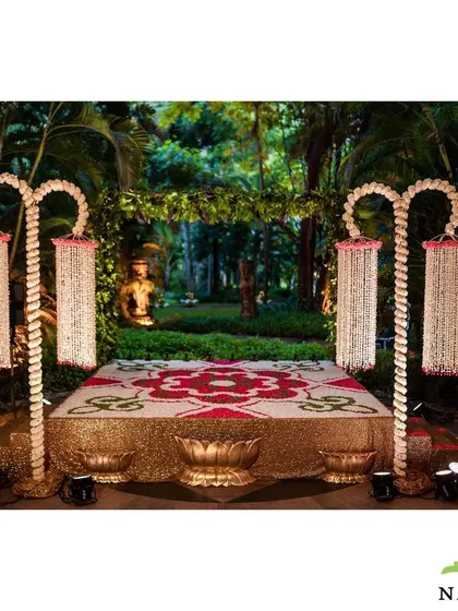 A beautiful floral rangoli and stage setup for an evening ceremony. The platform is decorated with a pattern made of flower petals, surrounded by traditional floral lamps.