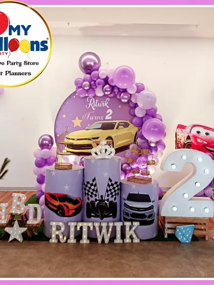 A cool Cars-themed second birthday party. The purple decor features a yellow sports car, Lightning McQueen, and a large light-up number '2'.