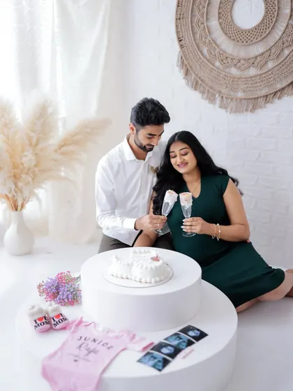 A sweet celebration for their baby boy. This photo captures the couple toasting with non-alcoholic drinks, surrounded by gender reveal props like a cake and baby clothes.