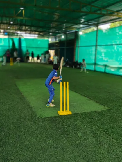 Another angle of a young batsman practicing indoors. The bright lighting and clear markings on the turf create a professional training environment.