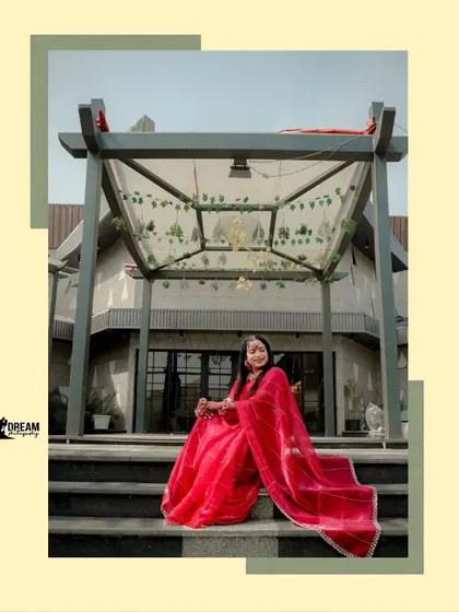 A beautiful shot of Ahana seated on the steps of the venue, her red saree spread out, creating a regal and elegant pose.