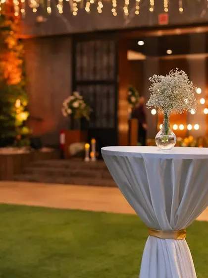 A cocktail table with a simple baby's breath arrangement, set against the warm glow of the evening reception.