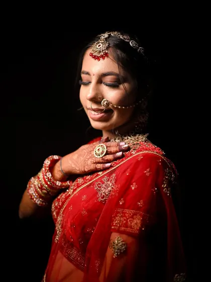 A dramatic portrait with a black background that makes her red outfit and glowing makeup pop. The soft smokey eyes and gentle smile create a captivating image.
