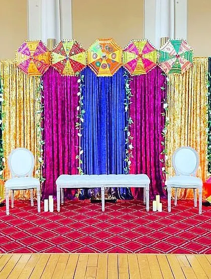 A vibrant stage with sequined and velvet drapes in jewel tones. The Rajasthani umbrellas add a traditional and colorful touch to this Sangeet setup.